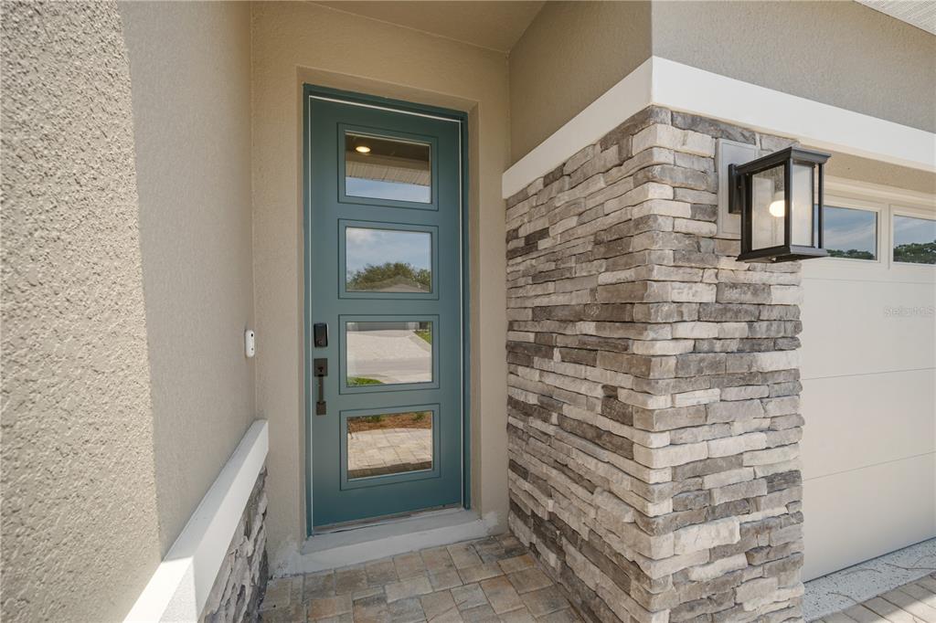 A teal front door with four glass panels sits beside a stone-accented garage wall — 9196 PLAYERS DRIVE, WEEKI WACHEE, FL