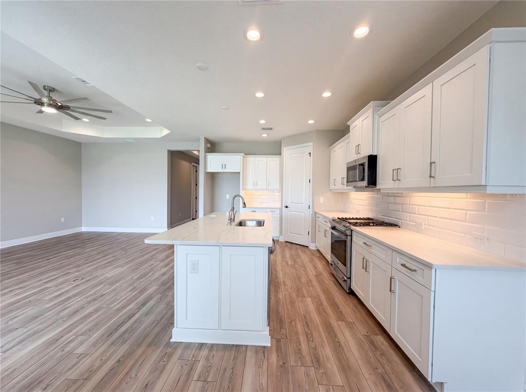 A modern kitchen features white cabinets, a central island, and light wood-look flooring — 10710 FALLING LEAF COURT, PARRISH, FL