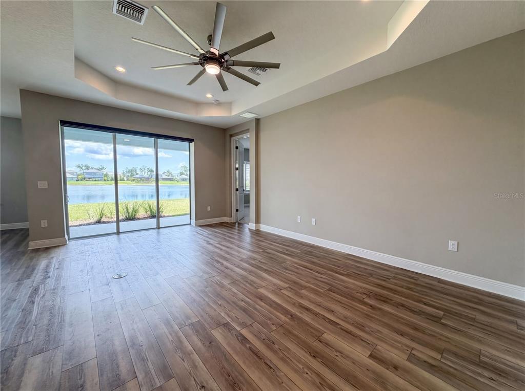 A living room features wood-look flooring, a tray ceiling with a fan, and sliding glass doors — 10710 FALLING LEAF COURT, PARRISH, FL