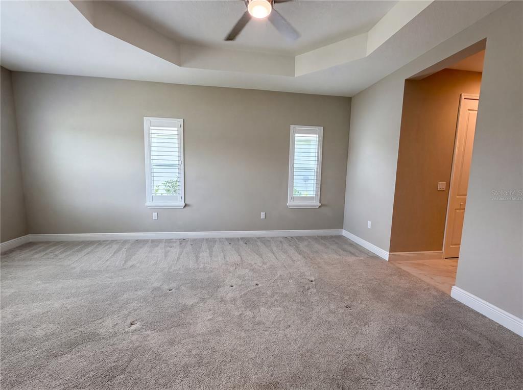 An empty bedroom features beige walls, gray carpeting, two windows with shutters, and a tray ceiling — 10710 FALLING LEAF COURT, PARRISH, FL