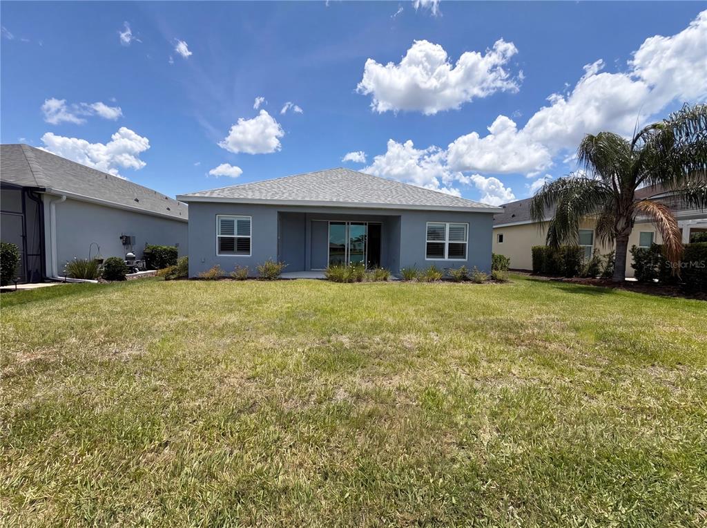The rear exterior of a gray single-story house features a lawn and a covered patio — 10710 FALLING LEAF COURT, PARRISH, FL