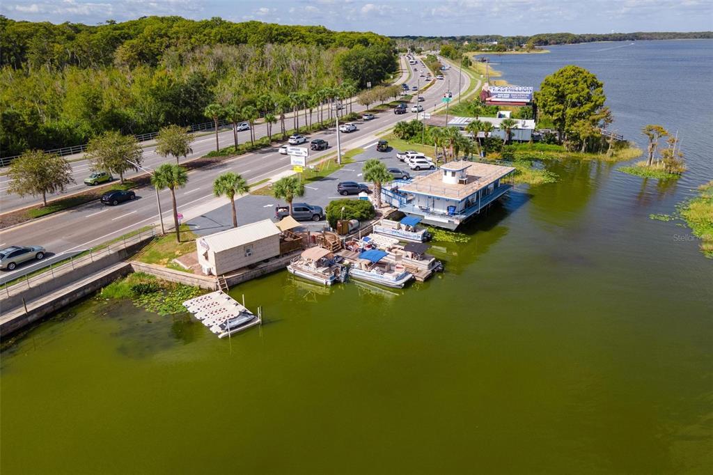 An aerial view shows a waterfront building and boat dock alongside a busy road — 1006 W BURLEIGH BOULEVARD, TAVARES, FL