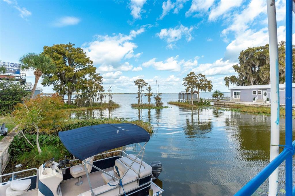 A pontoon boat is docked in a canal leading to a large lake with trees — 1006 W BURLEIGH BOULEVARD, TAVARES, FL