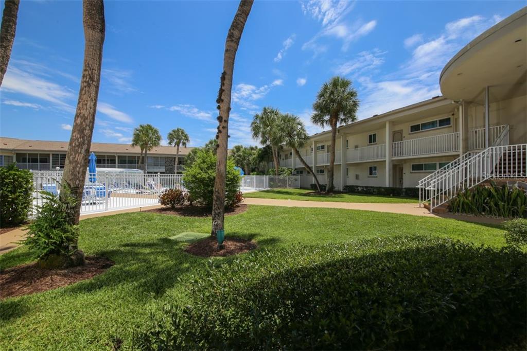 A grassy courtyard with palm trees, a swimming pool, and a multi-story apartment building exterior — 500 S WASHINGTON DRIVE UNIT 26B, SARASOTA, FL