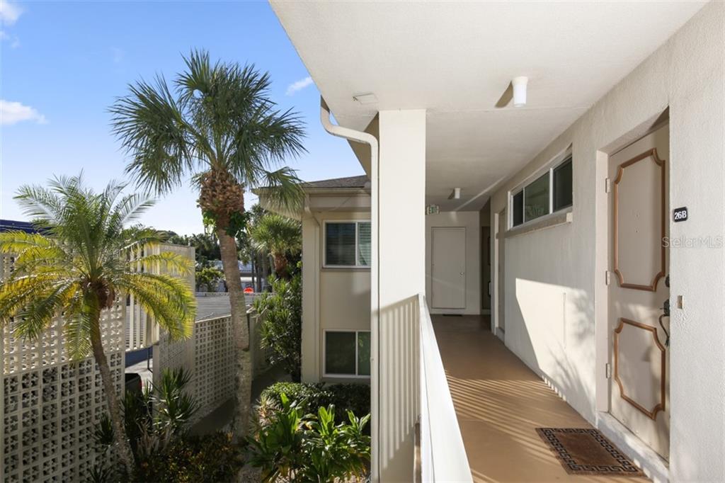 An exterior walkway leads to a tan door marked 26B beside a palm tree — 500 S WASHINGTON DRIVE UNIT 26B, SARASOTA, FL
