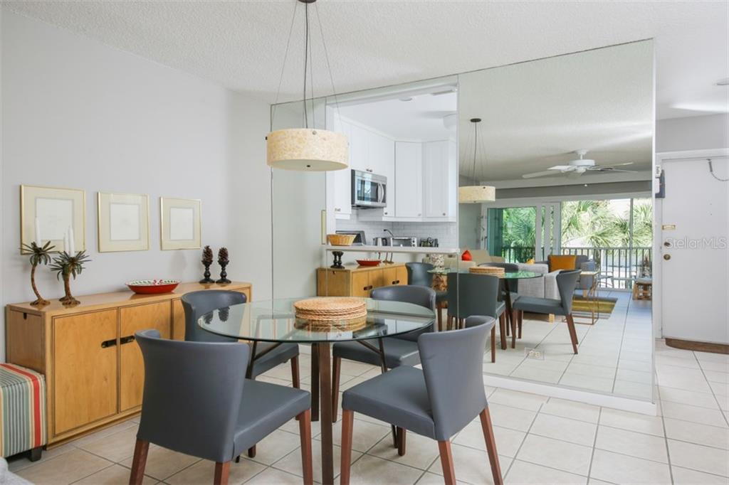 A dining area with a glass table, gray chairs, and a large mirrored wall — 500 S WASHINGTON DRIVE UNIT 26B, SARASOTA, FL