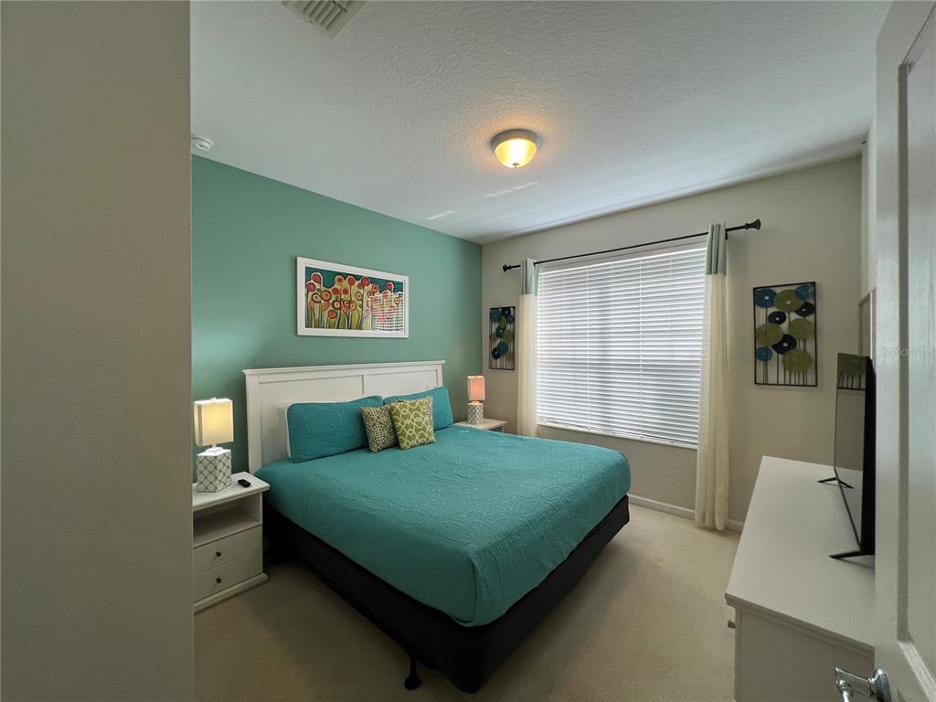 A bedroom features a teal accent wall, a king-sized bed, and a window with blinds — 2568 ARCHFELD BOULEVARD, KISSIMMEE, FL