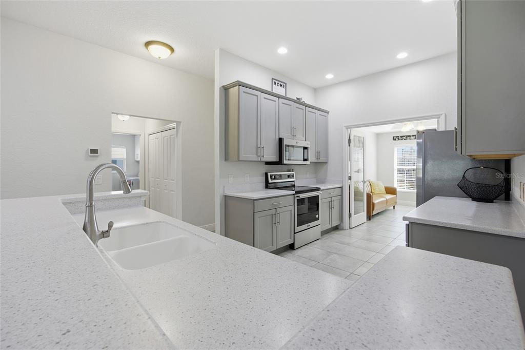 A kitchen features gray cabinets, white speckled countertops, stainless steel appliances, and tile flooring — 4846 AUDREY MARIE COURT, OXFORD, FL