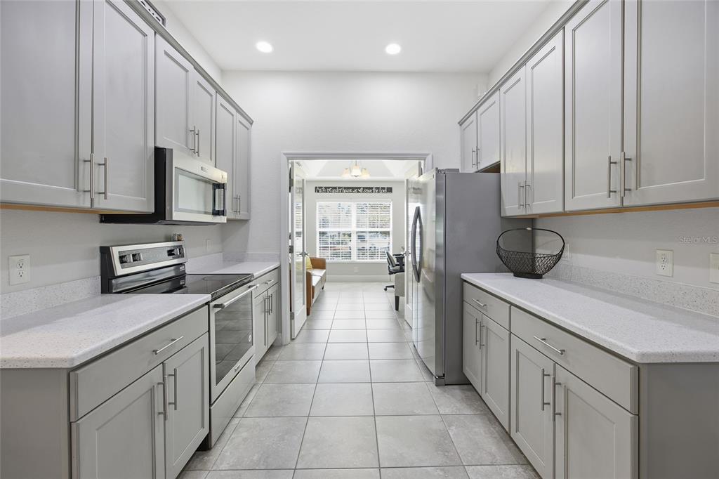 A galley-style kitchen features gray cabinets, white countertops, stainless steel appliances, and tile flooring — 4846 AUDREY MARIE COURT, OXFORD, FL
