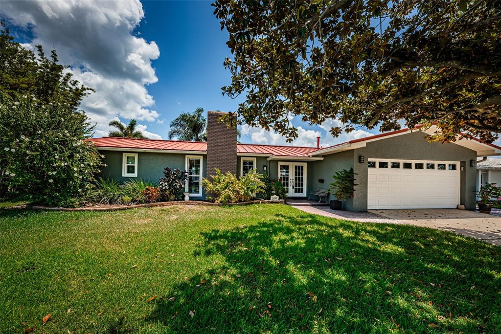 A single-story house with a red metal roof, gray stucco walls, and a white garage — 1496 49TH AVENUE NE, ST PETERSBURG, FL