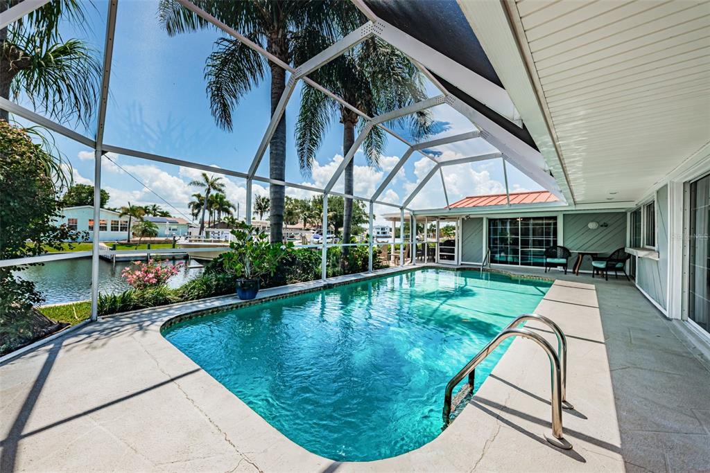 A swimming pool sits inside a screened-in lanai overlooking a canal with palm trees — 1496 49TH AVENUE NE, ST PETERSBURG, FL