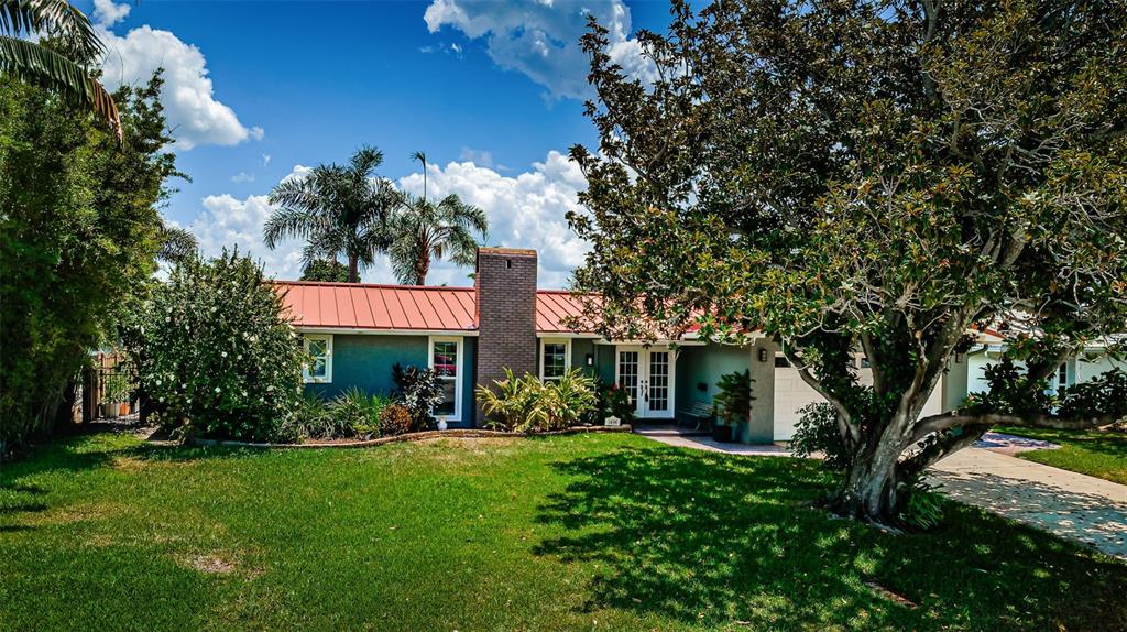 A single-story house with a red metal roof, brick chimney, and large front yard tree — 1496 49TH AVENUE NE, ST PETERSBURG, FL