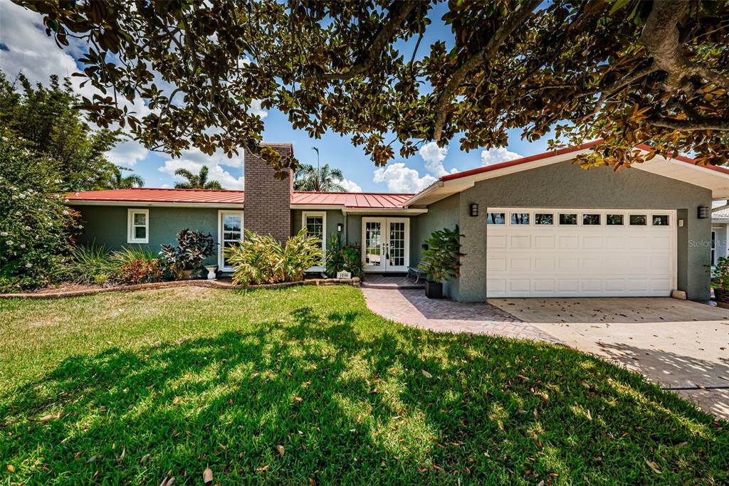 A single-story house with a red metal roof, gray exterior, and a white garage door — 1496 49TH AVENUE NE, ST PETERSBURG, FL