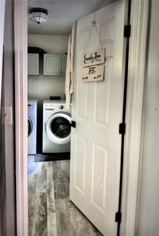 A laundry room with a front-loading washer and dryer, white cabinets, and wood-look flooring — 2535 NW 49TH PLACE, GAINESVILLE, FL