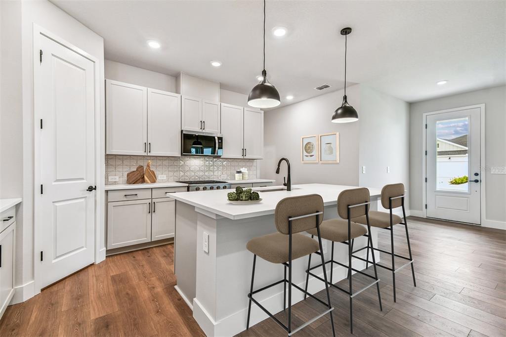 A modern kitchen features white cabinetry, a central island with bar seating, and wood flooring — 2836 MARRAKESH LANE, SARASOTA, FL