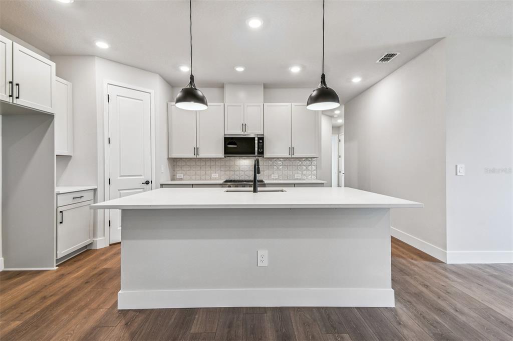 A modern kitchen features white cabinets, a central island with a sink, and pendant lighting — 2836 MARRAKESH LANE, SARASOTA, FL