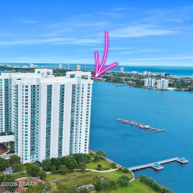 An aerial view shows a tall white residential building situated on a waterfront property — 231 RIVERSIDE DRIVE UNIT 2601-1, DAYTONA BEACH, FL