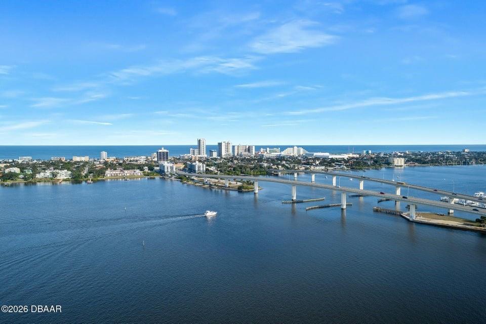 An aerial view shows a bridge spanning a wide river toward a coastal city skyline — 231 RIVERSIDE DRIVE UNIT 2601-1, DAYTONA BEACH, FL