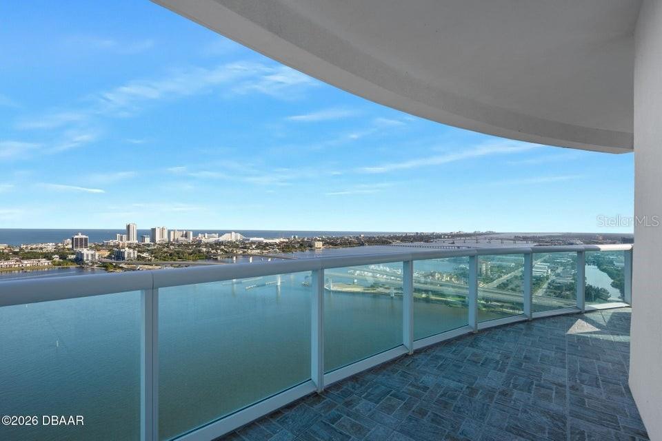 A curved balcony with glass railings overlooks a wide river and distant coastal city skyline — 231 RIVERSIDE DRIVE UNIT 2601-1, DAYTONA BEACH, FL