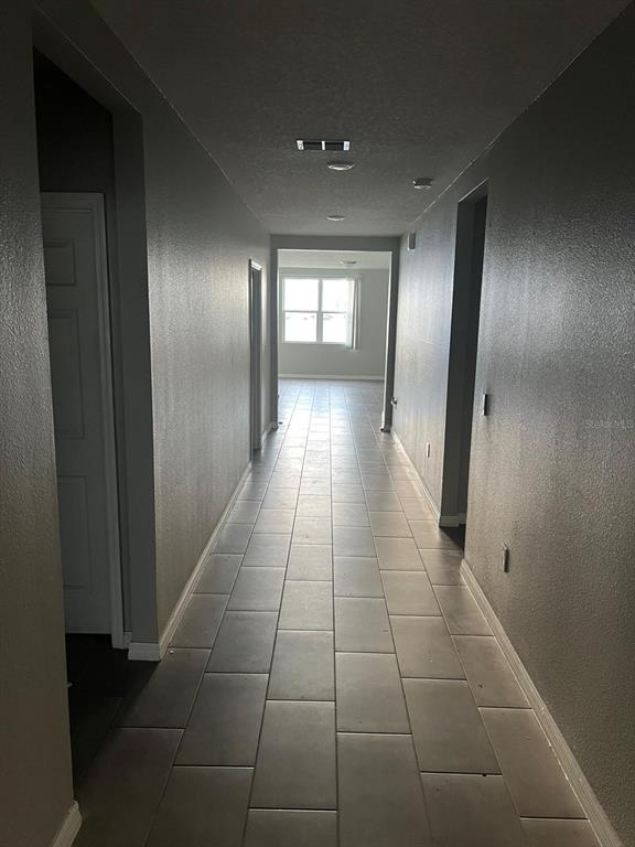 A long hallway with gray walls and light-colored rectangular floor tiles leads to a window — 528 MCKENNA DRIVE, WINTER HAVEN, FL