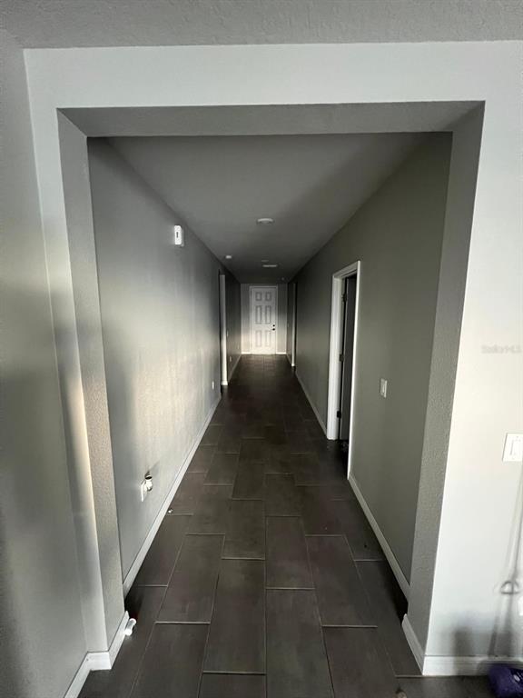 A long hallway features gray walls, dark rectangular floor tiles, and a white door at the end — 528 MCKENNA DRIVE, WINTER HAVEN, FL