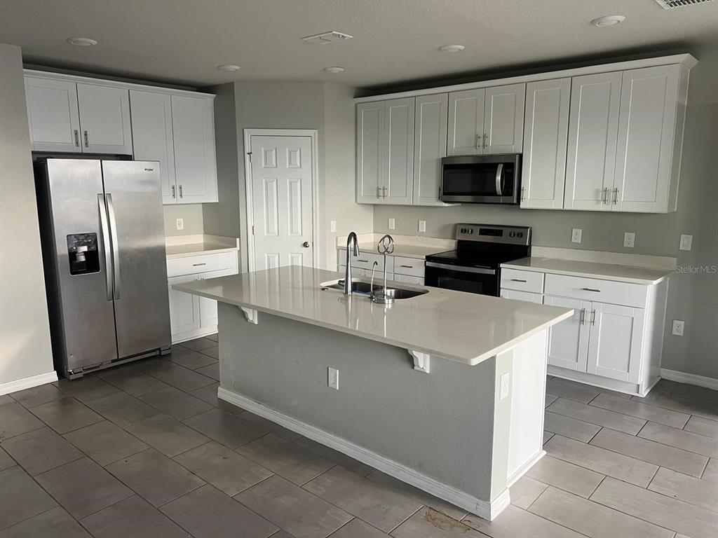 A kitchen features white cabinets, stainless steel appliances, a center island, and tile flooring — 528 MCKENNA DRIVE, WINTER HAVEN, FL