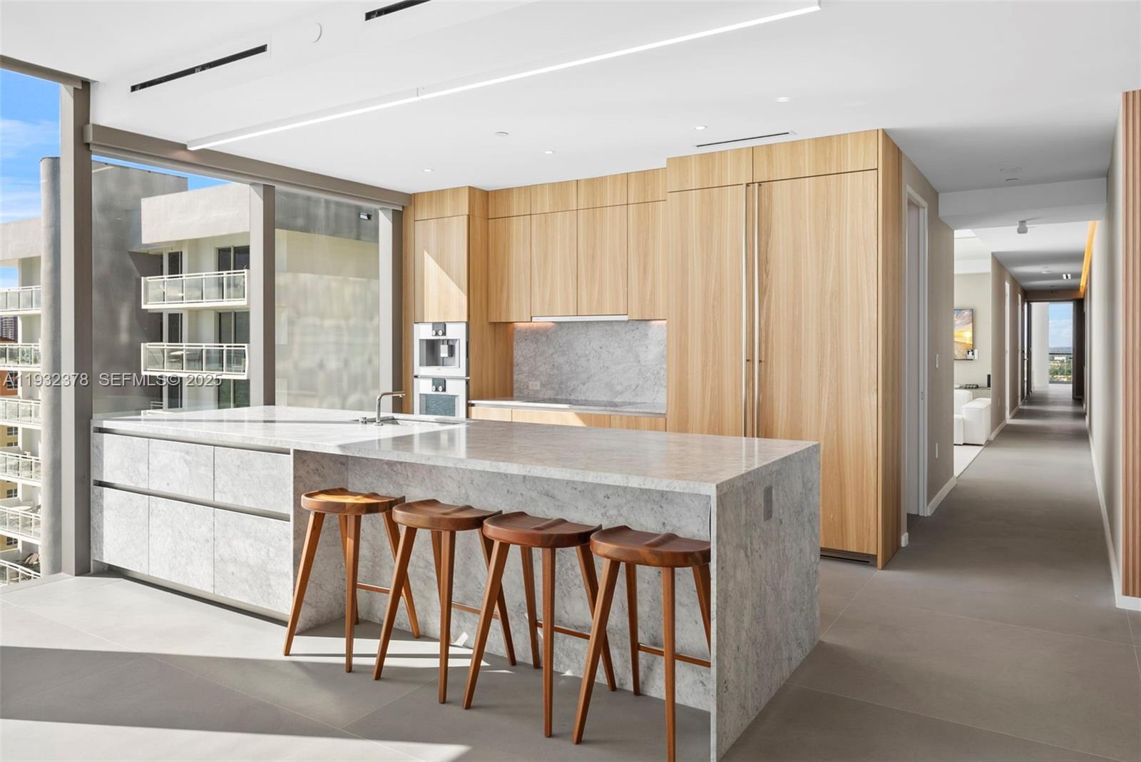 A modern kitchen features a marble island with wooden stools and light wood cabinetry — 2000 S Ocean Dr # 18B, Hallandale Beach FL 33009, HALLANDALE BEACH, FL