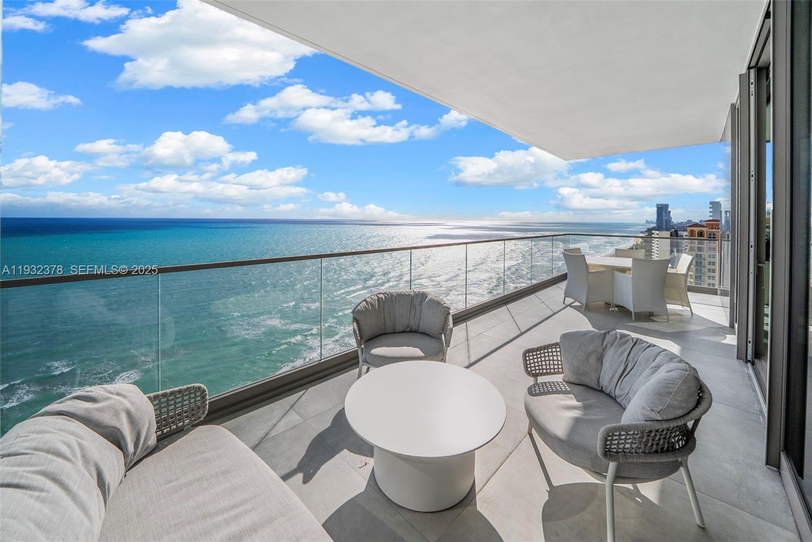 A spacious balcony features modern outdoor furniture overlooking the ocean and a coastal skyline — 2000 S Ocean Dr # 18B, Hallandale Beach FL 33009, HALLANDALE BEACH, FL