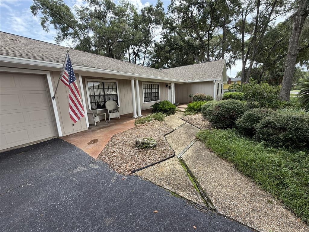 A tan house with a flag, a concrete walkway, and a driveway under large trees — 3925 SE 17TH STREET, OCALA, FL