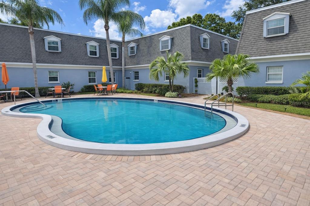A blue building with a mansard roof overlooks a kidney-shaped swimming pool and patio — 1712 BELLEAIR FOREST DRIVE UNIT A, BELLEAIR, FL