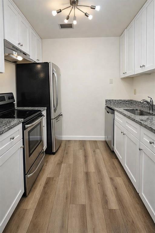 A narrow kitchen features white cabinets, stainless steel appliances, granite countertops, and wood-look flooring — 1712 BELLEAIR FOREST DRIVE UNIT A, BELLEAIR, FL