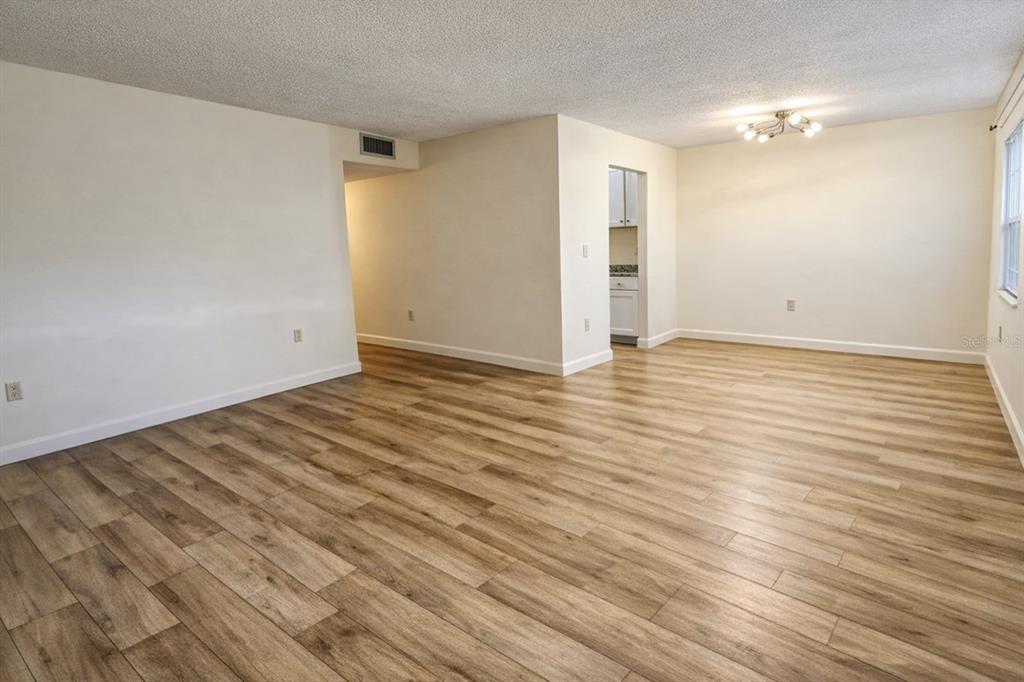 An empty room with light-colored walls, wood-look flooring, and a ceiling light fixture — 1712 BELLEAIR FOREST DRIVE UNIT A, BELLEAIR, FL