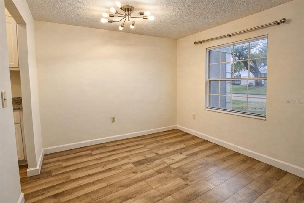 An empty dining room with wood-look flooring, a modern light fixture, and a single window — 1712 BELLEAIR FOREST DRIVE UNIT A, BELLEAIR, FL