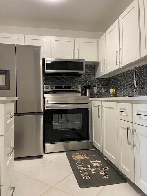 A kitchen features white cabinets, stainless steel appliances, and a dark tile backsplash — 1011 Berkshire A # 1011, Deerfield Beach FL 33442, DEERFIELD BEACH, FL