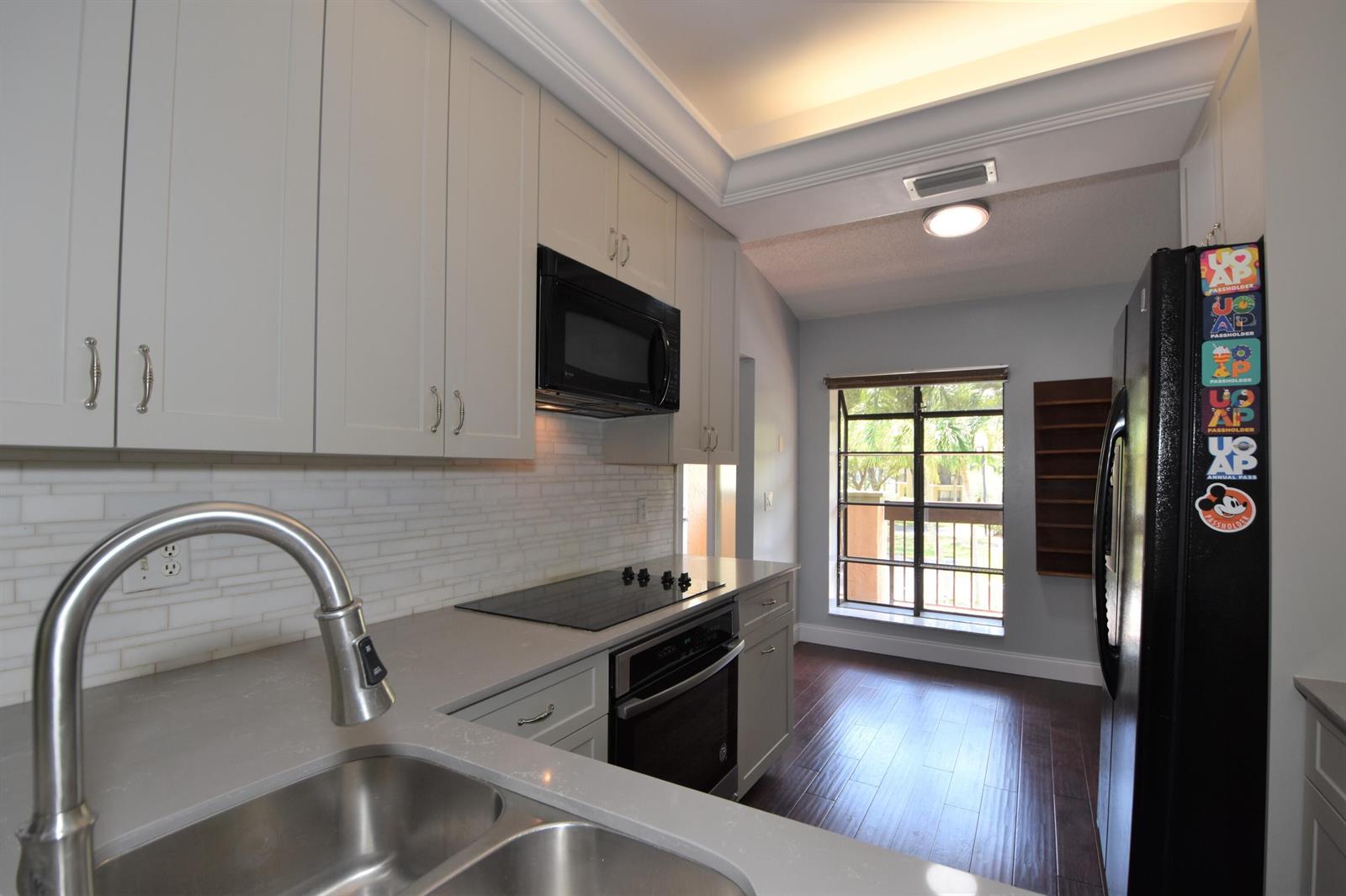 A kitchen with white cabinets, stainless steel sink, black appliances, and dark wood flooring — 5087 Oakhill Lane, Delray Beach FL 33484, DELRAY BEACH, FL