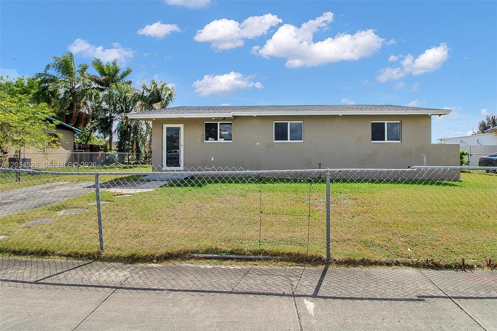 A single-story house with a beige exterior and a chain-link fence in the front yard — 12840 SW 268th St, Homestead FL 33032, HOMESTEAD, FL