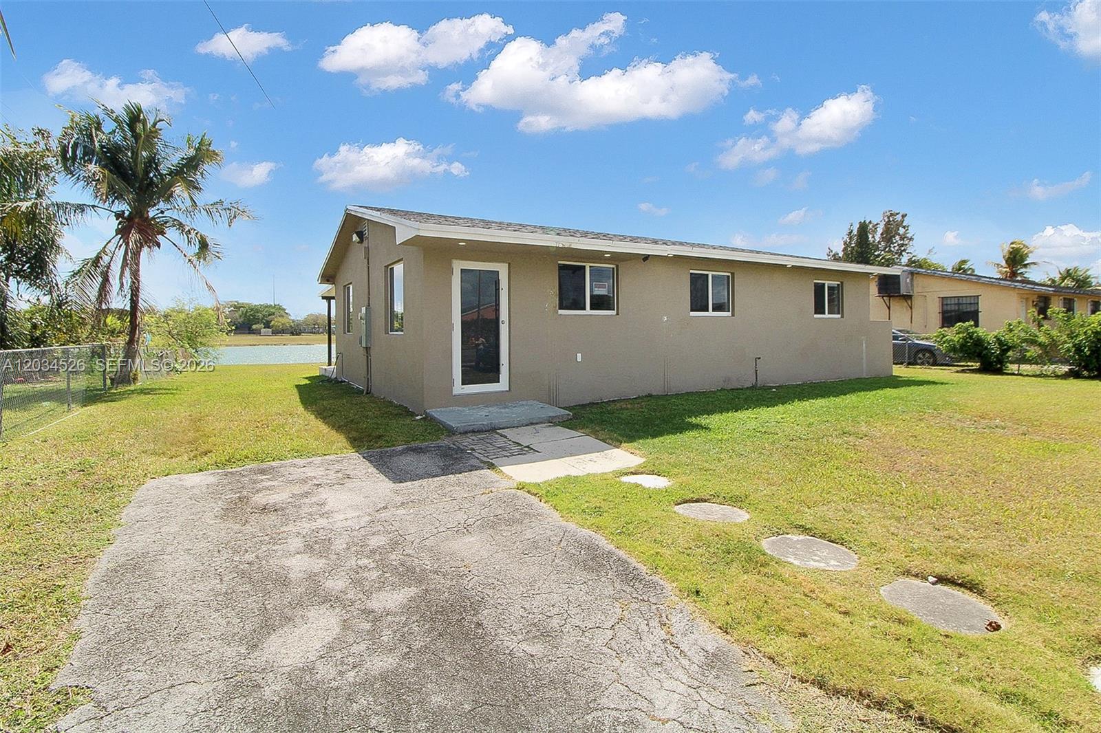 A tan, single-story house with a concrete driveway and a view of a lake — 12840 SW 268th St, Homestead FL 33032, HOMESTEAD, FL