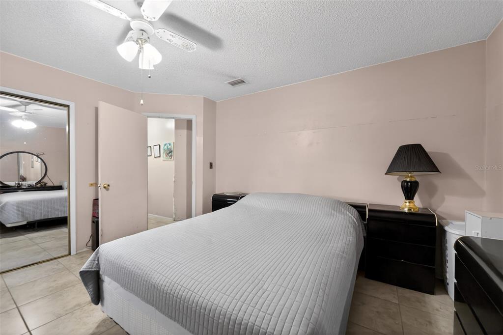 A bedroom features a bed, a ceiling fan, a table lamp, and tiled flooring — 470 WURST ROAD, OCOEE, FL