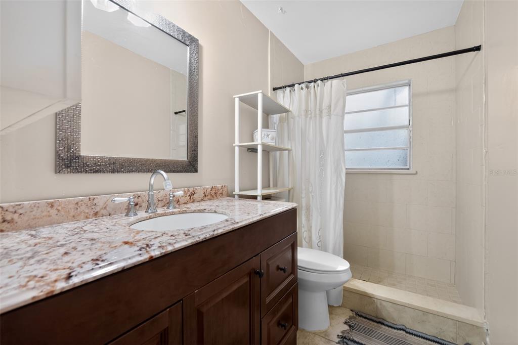 A bathroom features a granite vanity, dark wood cabinets, a mirror, and a tiled shower — 470 WURST ROAD, OCOEE, FL