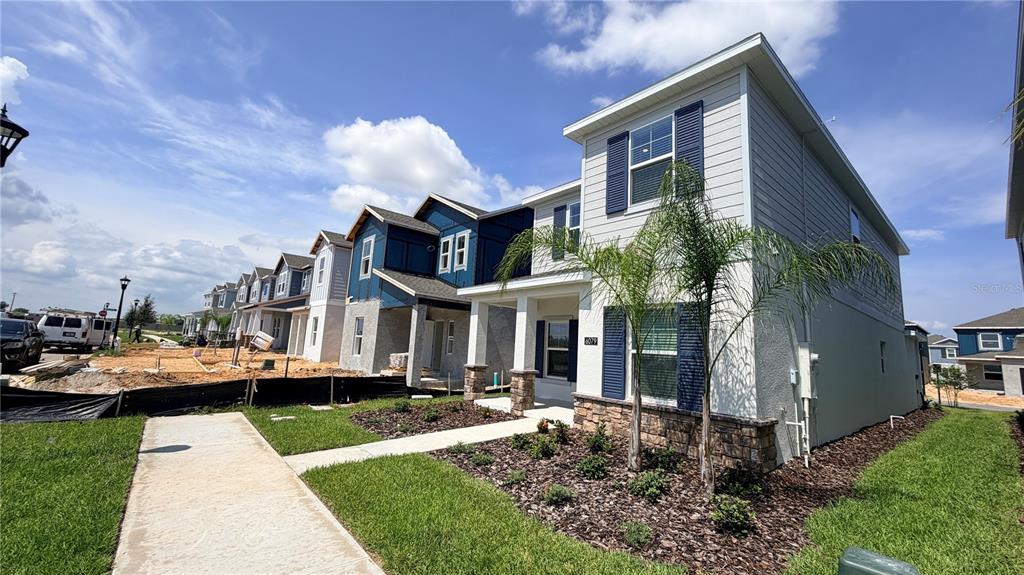 A row of modern two-story townhomes with light siding and blue shutters under a blue sky — 6079 WELLBEING WAY, CLERMONT, FL