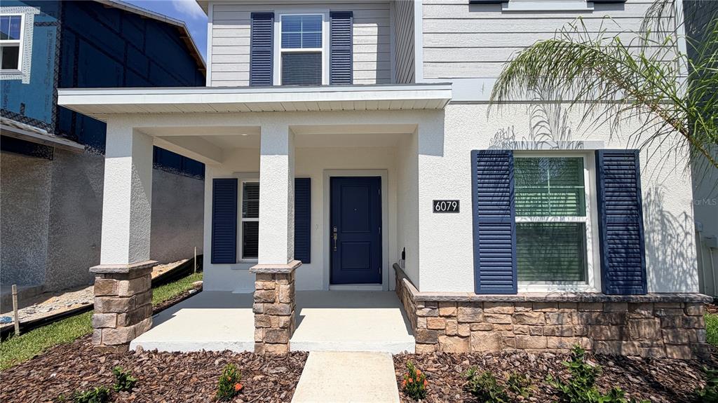 A front exterior view of a house featuring a covered porch, stone accents, and blue shutters — 6079 WELLBEING WAY, CLERMONT, FL