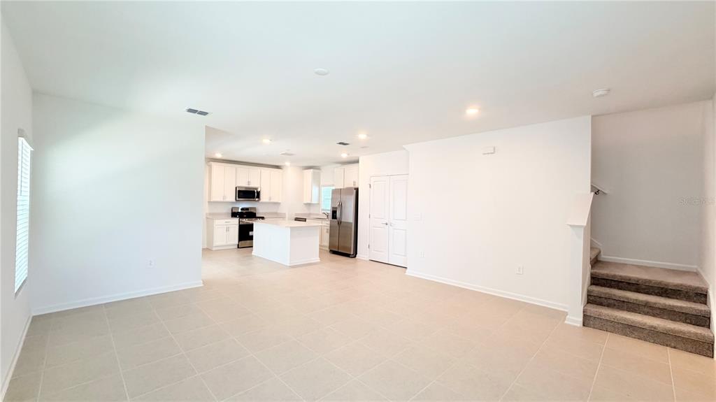 An open-concept kitchen with white cabinets and stainless steel appliances overlooks a tiled living area — 6079 WELLBEING WAY, CLERMONT, FL