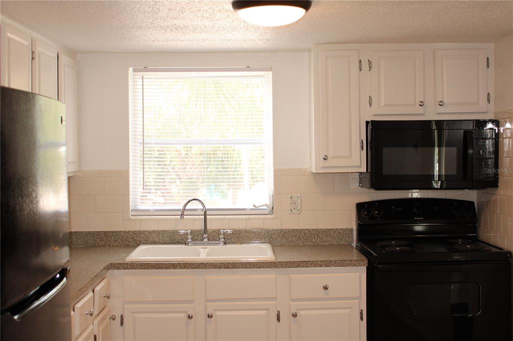 A kitchen features white cabinets, a black microwave and stove, and a white sink — 2423 60TH AVENUE W UNIT K29, BRADENTON, FL