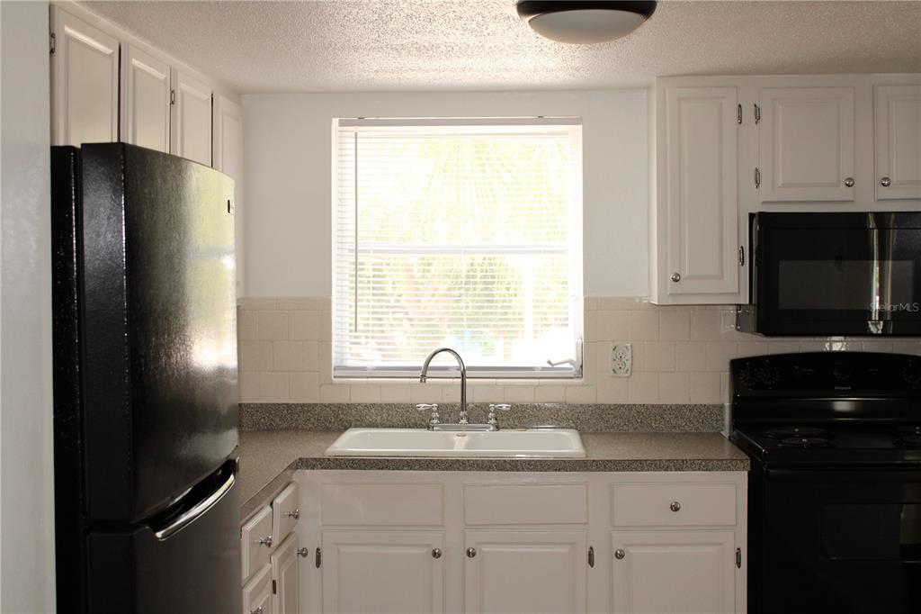 A kitchen features white cabinets, black appliances, a double sink, and a window above — 2423 60TH AVENUE W UNIT K29, BRADENTON, FL