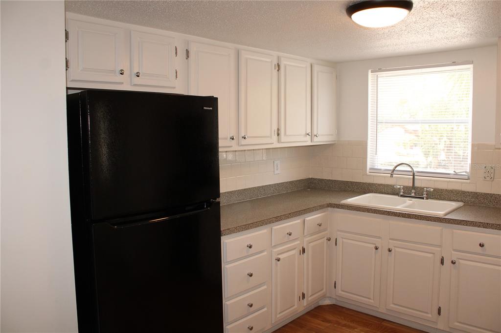 A kitchen features white cabinets, a black refrigerator, a double sink, and gray countertops — 2423 60TH AVENUE W UNIT K29, BRADENTON, FL