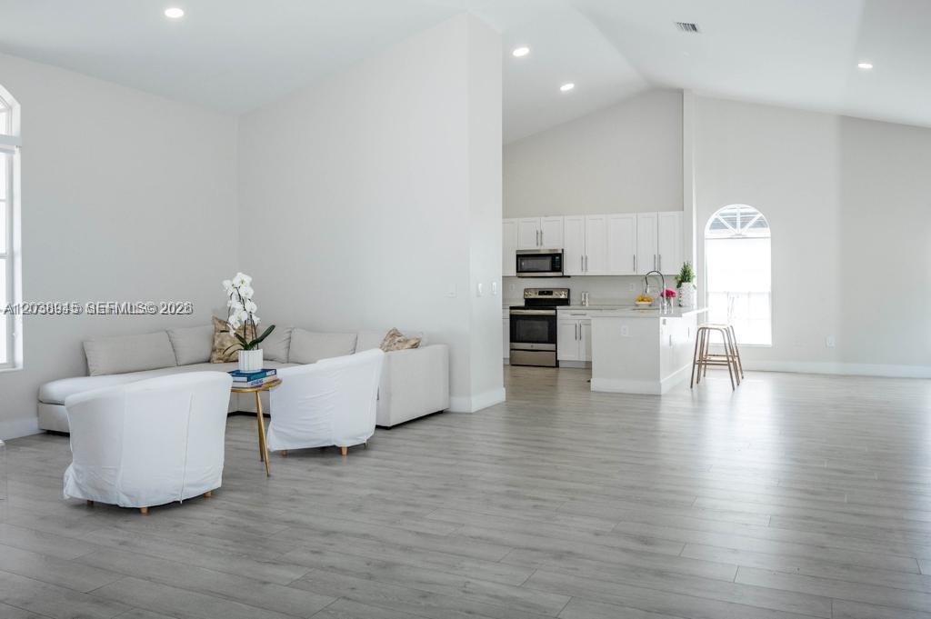 A bright, open-concept living room flows into a kitchen with white cabinetry and light flooring — 8325 NW 161st Ter, Miami Lakes FL 33016, MIAMI LAKES, FL