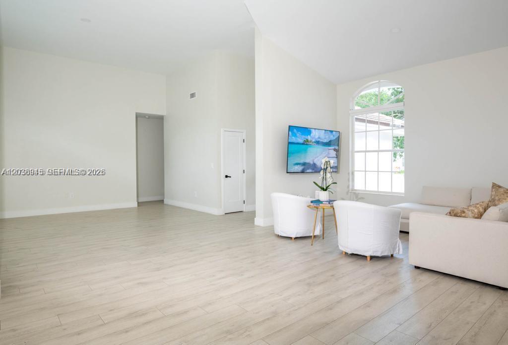 A bright living room features light wood-look flooring, white walls, and a wall-mounted television — 8325 NW 161st Ter, Miami Lakes FL 33016, MIAMI LAKES, FL