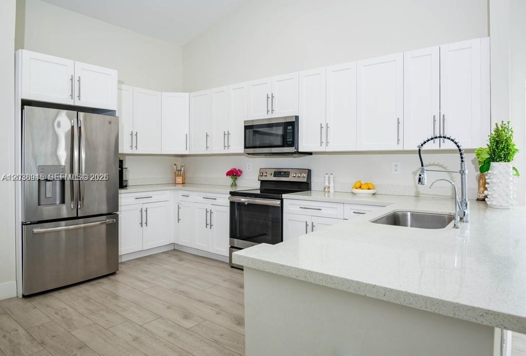 A modern kitchen features white cabinets, stainless steel appliances, and light-colored quartz countertops — 8325 NW 161st Ter, Miami Lakes FL 33016, MIAMI LAKES, FL