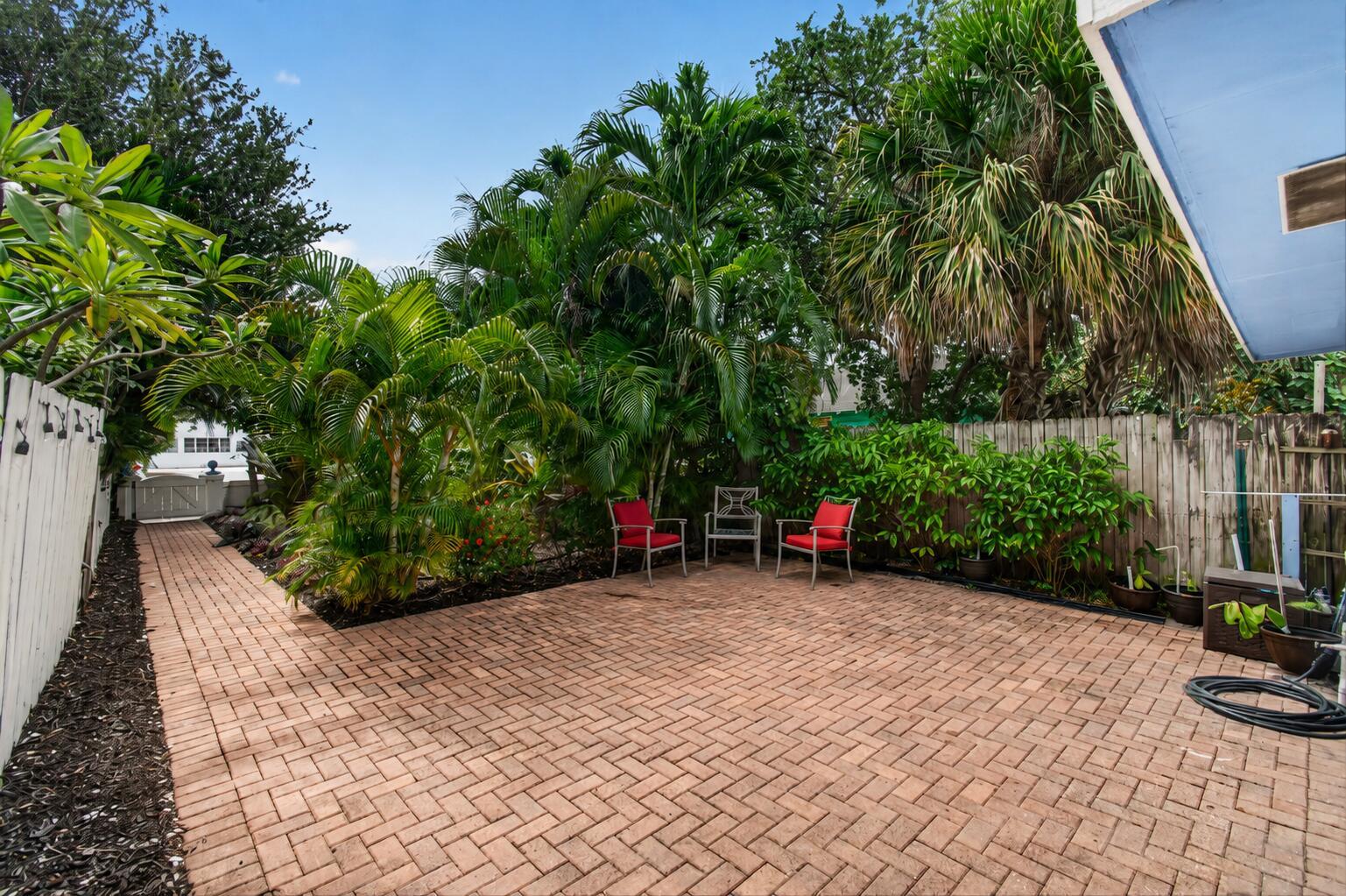 A brick patio features three chairs and lush tropical landscaping enclosed by a wooden fence — 227 N M Street, FL 33460, FL