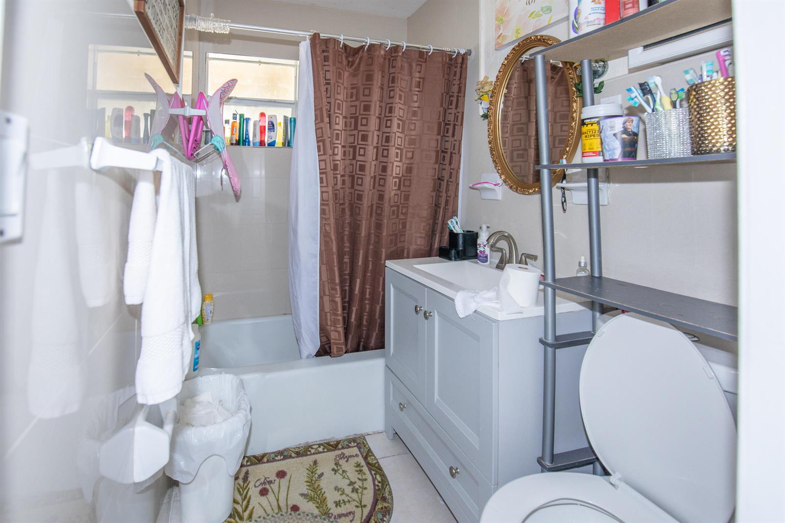 A small bathroom features a gray vanity, a shower-tub combination with a brown curtain, and shelving — 922 S Dixie Street, FL 33460, FL